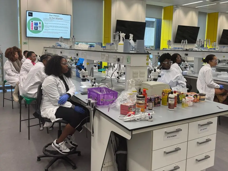 TRIYBE In the Lab workshop: participants in lab coats at microscope benches, with Black hair care products on the bench