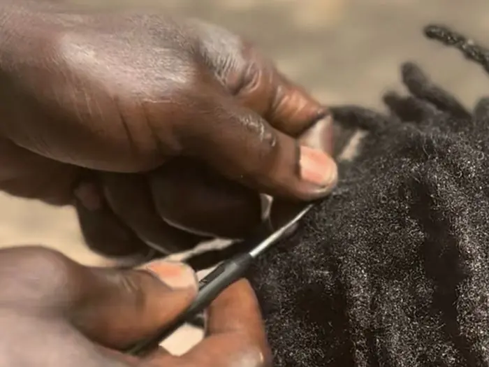 Hands carefully sectioning and maintaining locs, passing on hair heritage skills