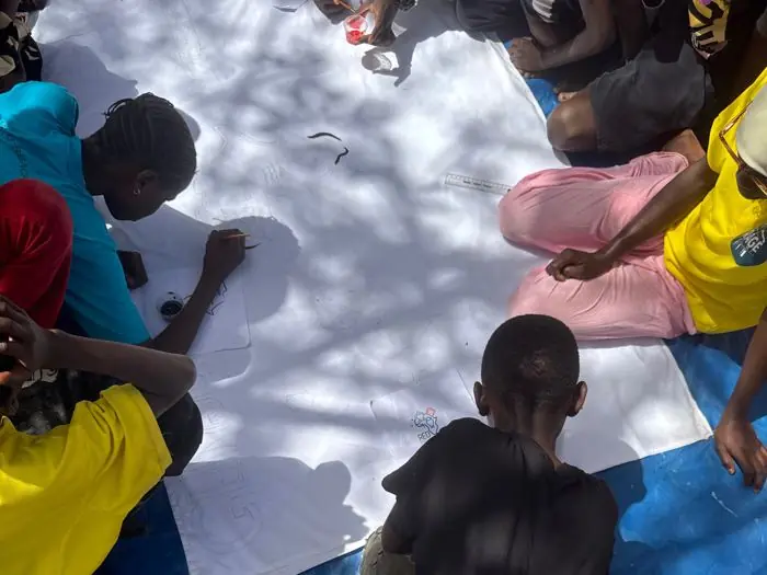 Young people painting a large community banner together at The Gunjur Project, The Gambia